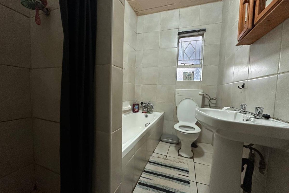 A compact bathroom featuring a bathtub, pedestal basin, and toilet, with floor-to-ceiling wall tiling and a small window for natural light.