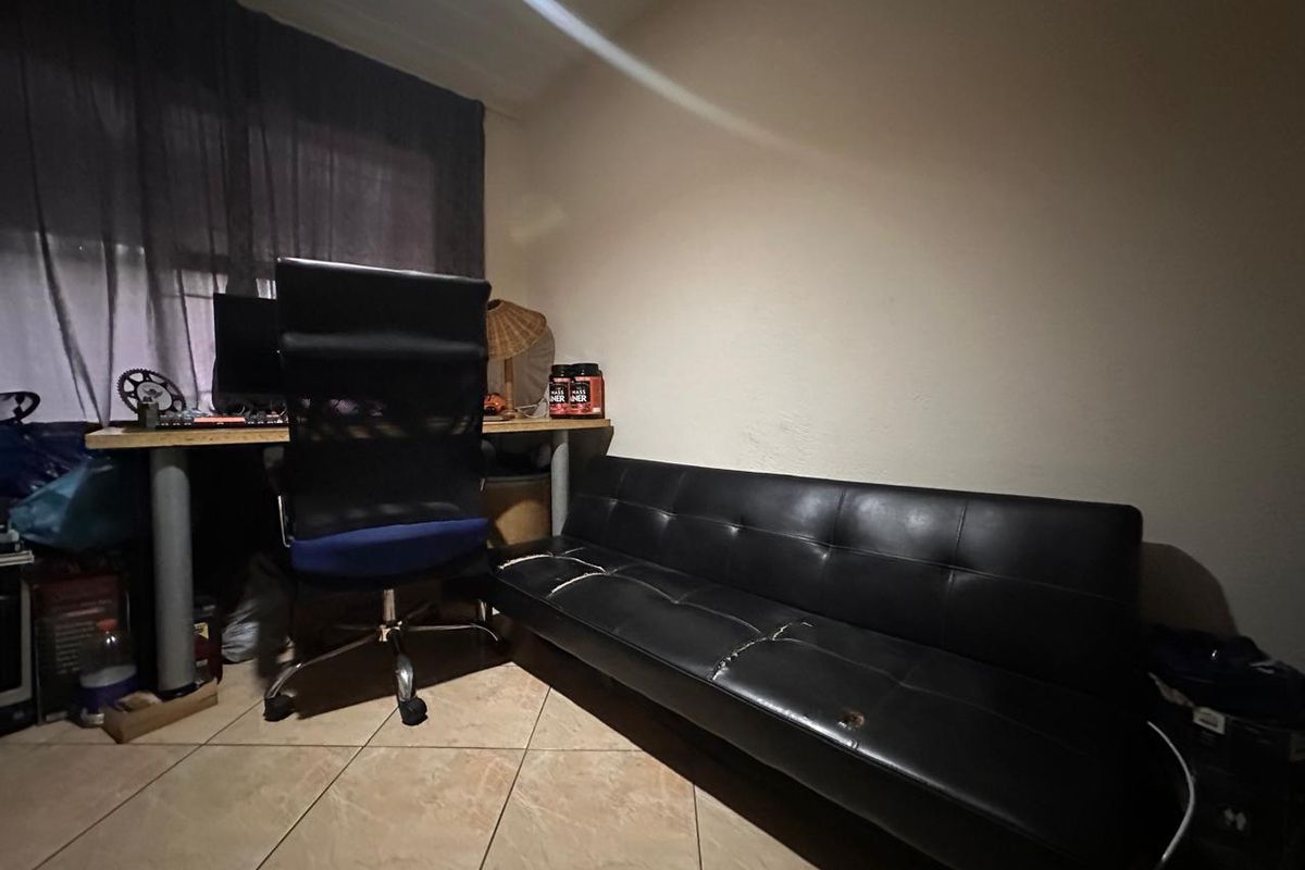 A small room featuring tiled flooring, currently utilized as a home office and lounge area.