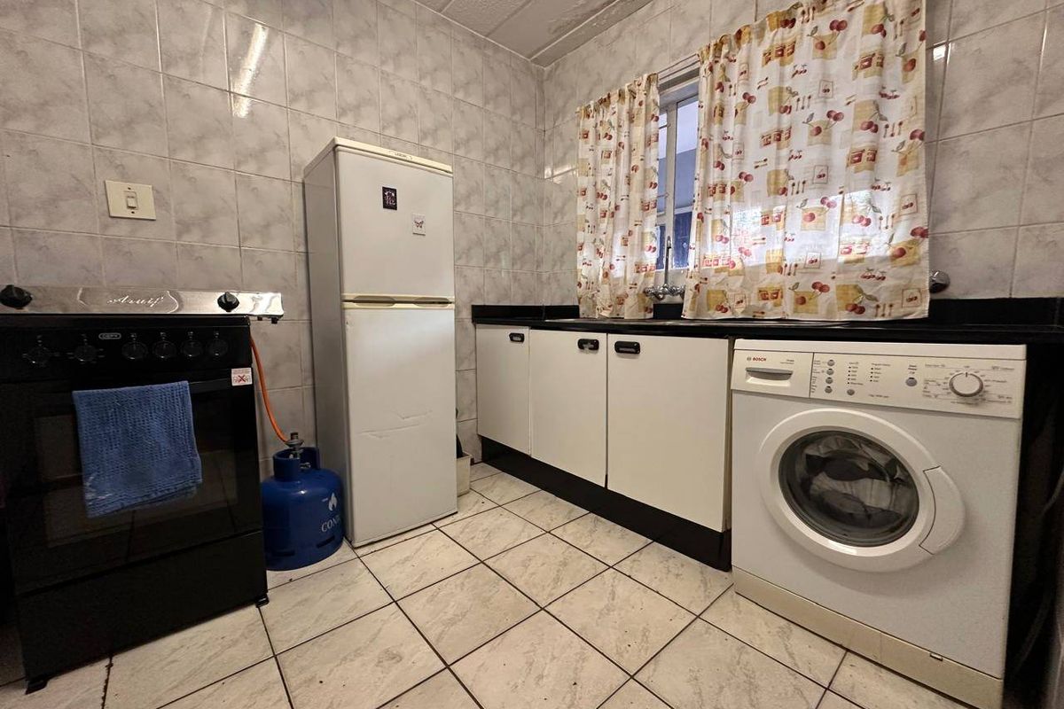 A functional kitchen featuring tiled walls, built-in cabinetry, a black countertop, and dedicated space for laundry appliances.