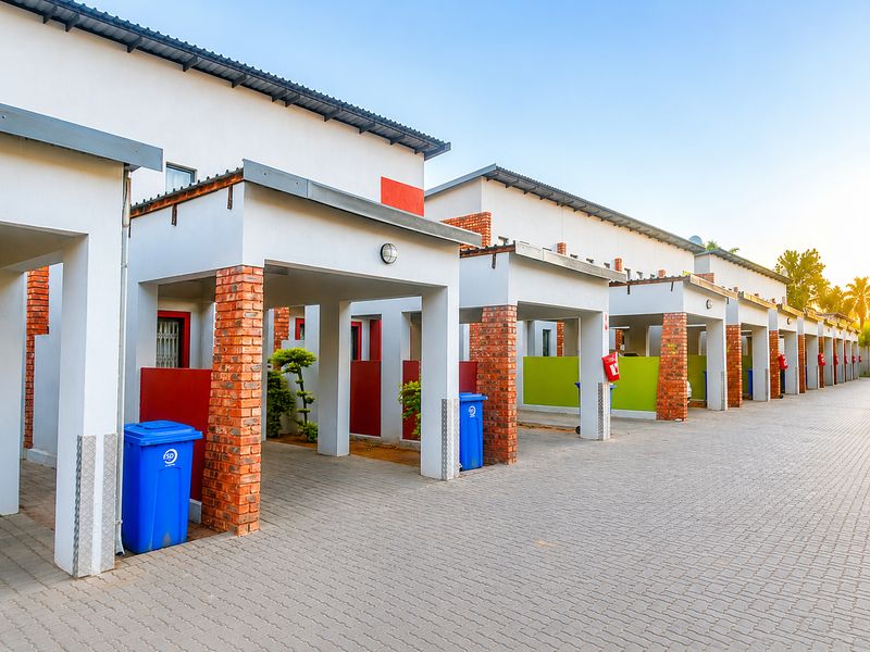 A row of modern apartment units featuring covered carports, brick pillar detailing, and a paved driveway area.