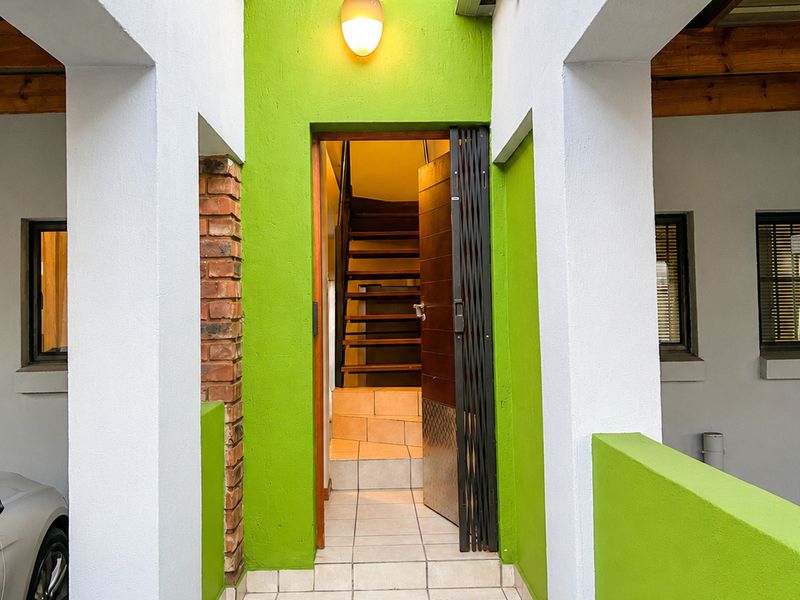 Entrance area featuring tiled steps leading to an interior staircase, accented by a bright green facade and exposed brick detailing.
