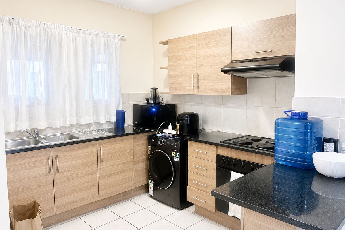 A functional kitchen featuring light wood-finish cabinetry, dark granite countertops, a built-in oven with hob, and tiled flooring.