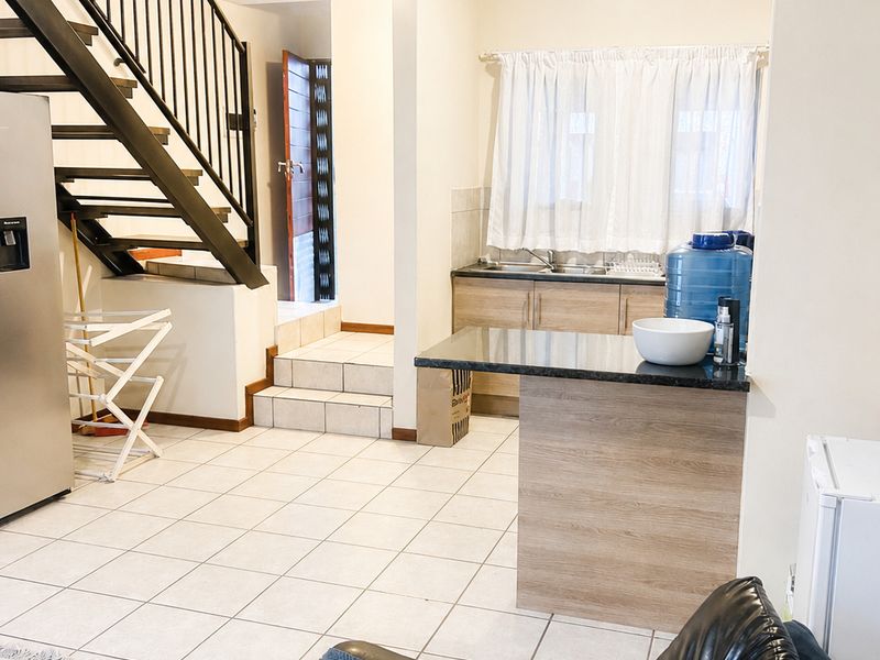 Open plan living area featuring a staircase with metal balustrade and a functional kitchen with granite countertops and tiled flooring.