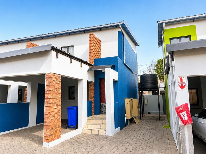 Front elevation of a modern apartment unit featuring a covered carport, paved driveway, and exterior water storage tank.