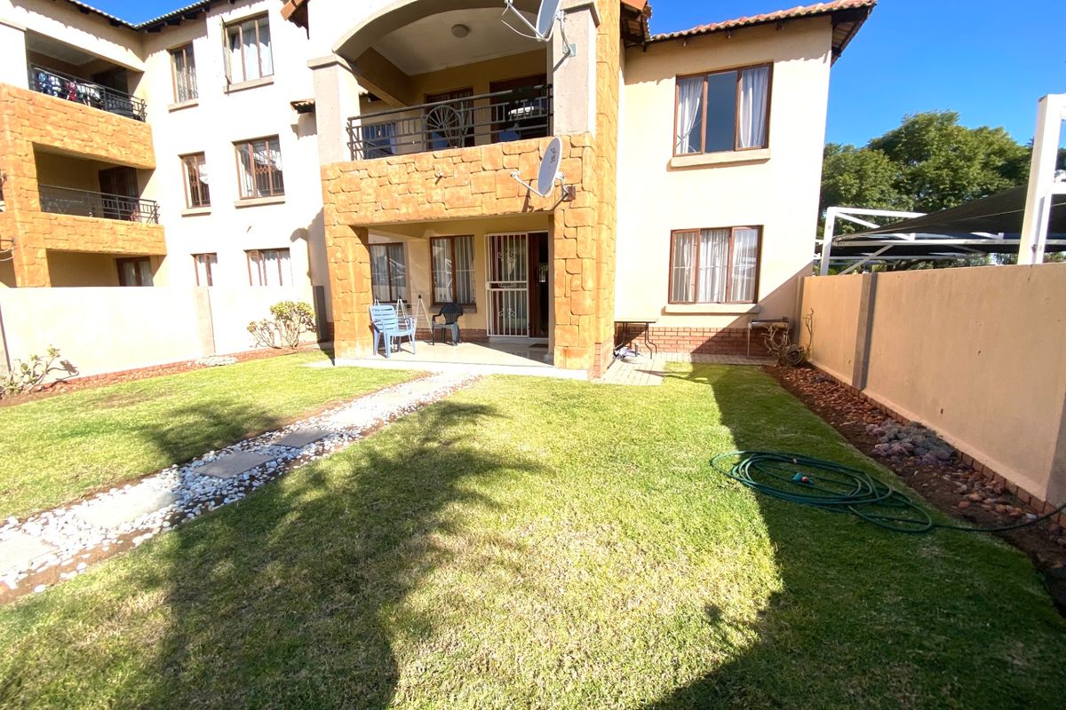 Rear view of a multi-story townhouse featuring a private garden, covered patio, and balcony with stone cladding accents.