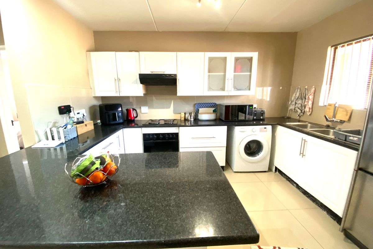 A functional kitchen featuring white cabinetry, dark granite countertops, a built-in oven with extractor fan, and an integrated washing machine space.