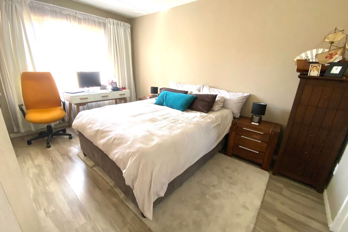 A well-lit bedroom featuring light-toned wood-look flooring and a large window with curtains, providing a comfortable and functional living space.