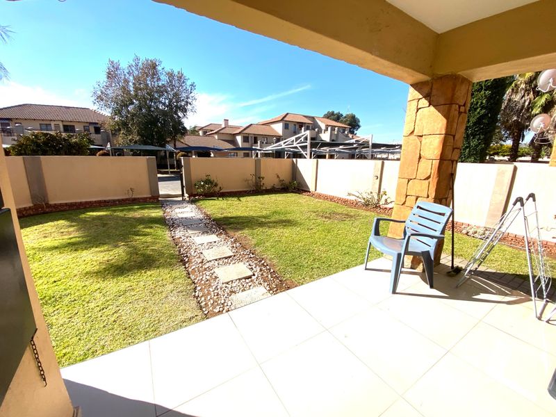 A covered patio area overlooking a private garden with a stone-clad pillar and tiled flooring, providing a pleasant outdoor space.