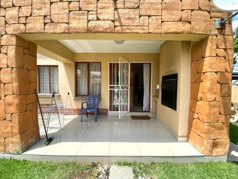 Covered patio area featuring stone cladding, tiled flooring, and a built-in braai, providing a functional outdoor entertainment space.