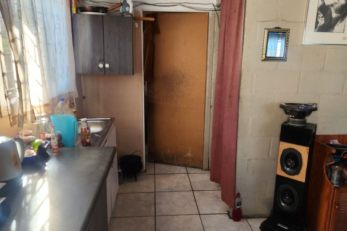 A small kitchen area featuring tiled flooring, built-in cabinetry, and a sink, currently showing significant signs of wear and dated finishes.