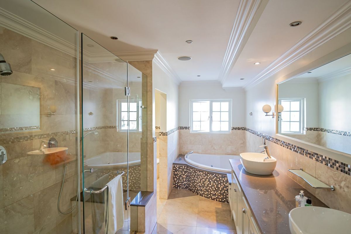 Spacious modern bathroom featuring a glass-enclosed shower, corner bathtub, double vanity with stone countertop, and elegant mosaic tile detailing.