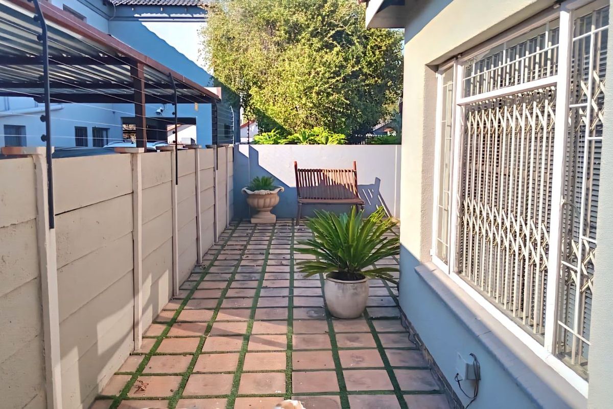 A side exterior walkway featuring paved flooring, a precast concrete boundary wall with electric fencing, and secure window bars.