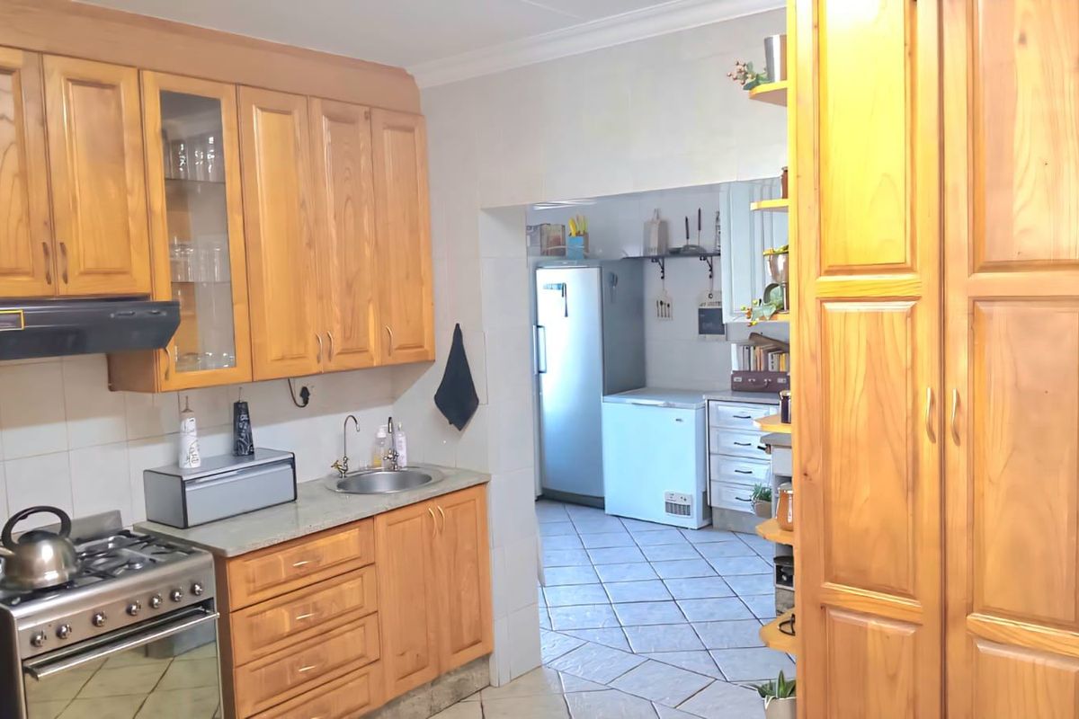 A functional kitchen featuring warm-toned wooden cabinetry, a gas stove with extractor fan, and tiled flooring, with an adjacent scullery area for additional storage.