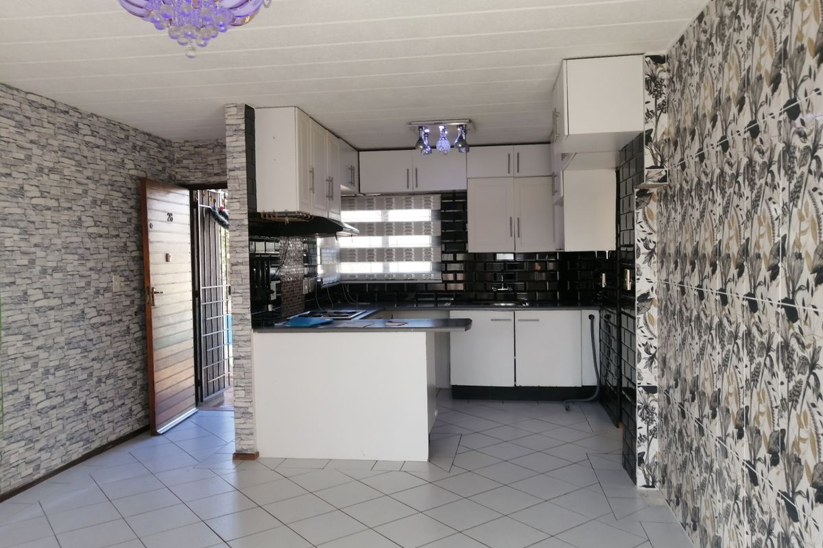 A functional kitchen area featuring white built-in cabinetry, dark subway tile backsplash, and tiled flooring, offering a blank canvas for modern updates.