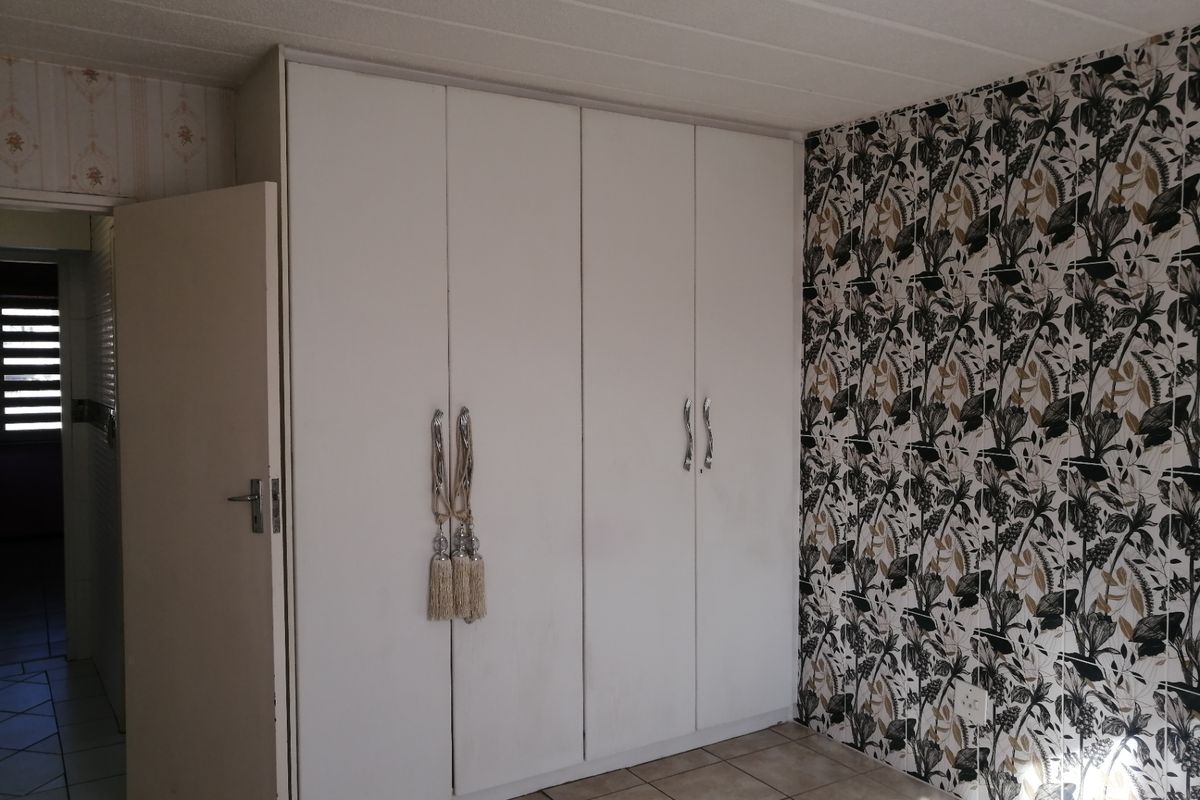A bedroom featuring built-in cupboards, tiled flooring, and decorative wallpaper, offering a blank canvas for potential interior updates.