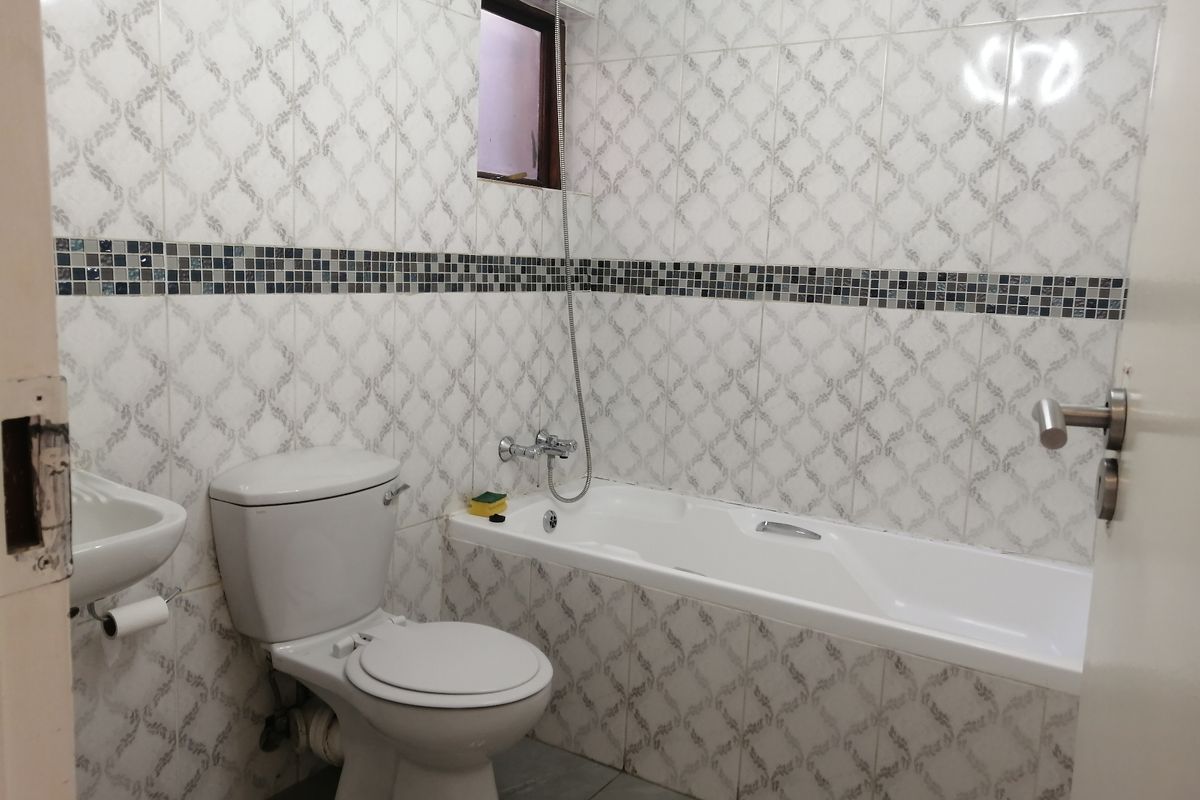 A functional bathroom featuring a bathtub with a handheld shower, a wall-mounted basin, and decorative tiled walls with a mosaic accent border.