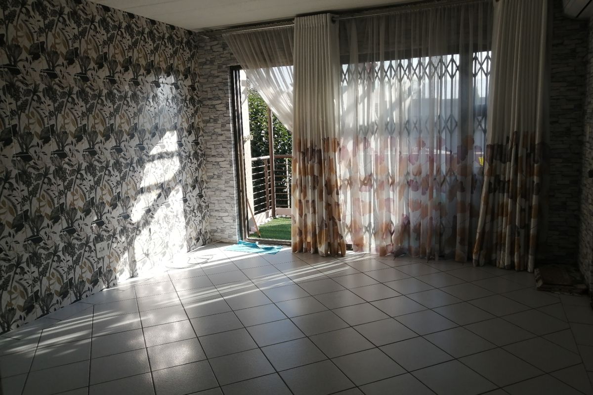 Spacious living area featuring tiled flooring, patterned wallpaper, and a sliding glass door providing access to an outdoor balcony.