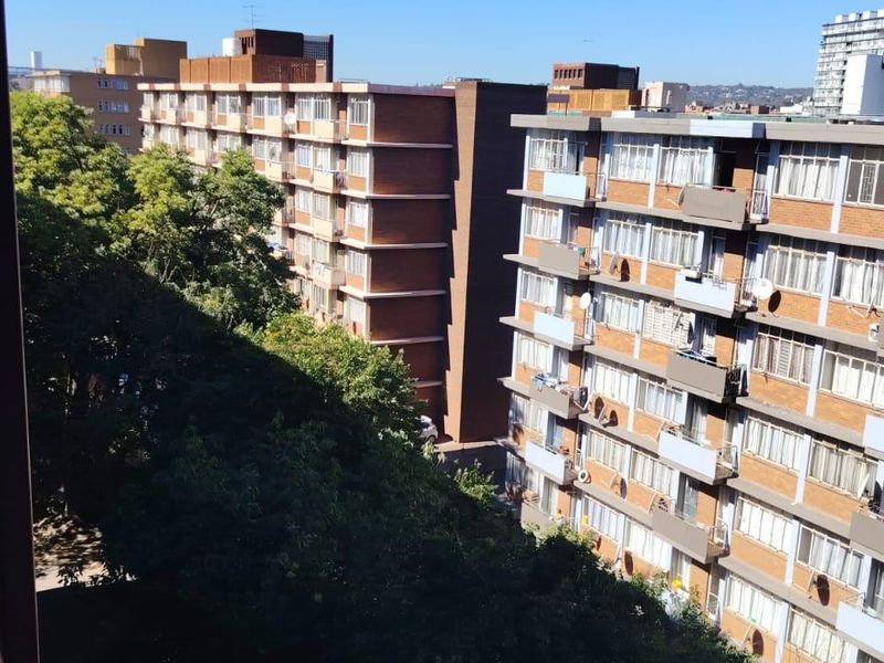 An elevated view from a balcony overlooking the surrounding apartment complex and mature trees in a residential urban setting.
