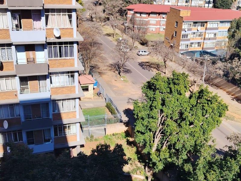 An elevated aerial view showing the exterior facade of a brick apartment building, surrounding street infrastructure, and mature trees.