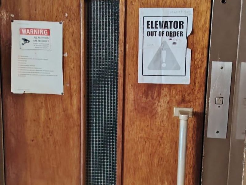 A view of an elevator door featuring a metal handle, door closer, and signage indicating the elevator is currently out of order.