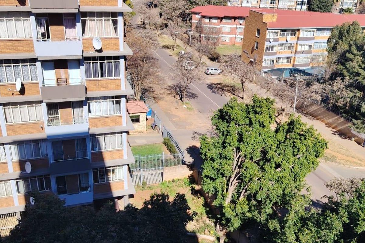 An elevated aerial view showing the exterior facade of a brick apartment building, surrounding street infrastructure, and mature trees.