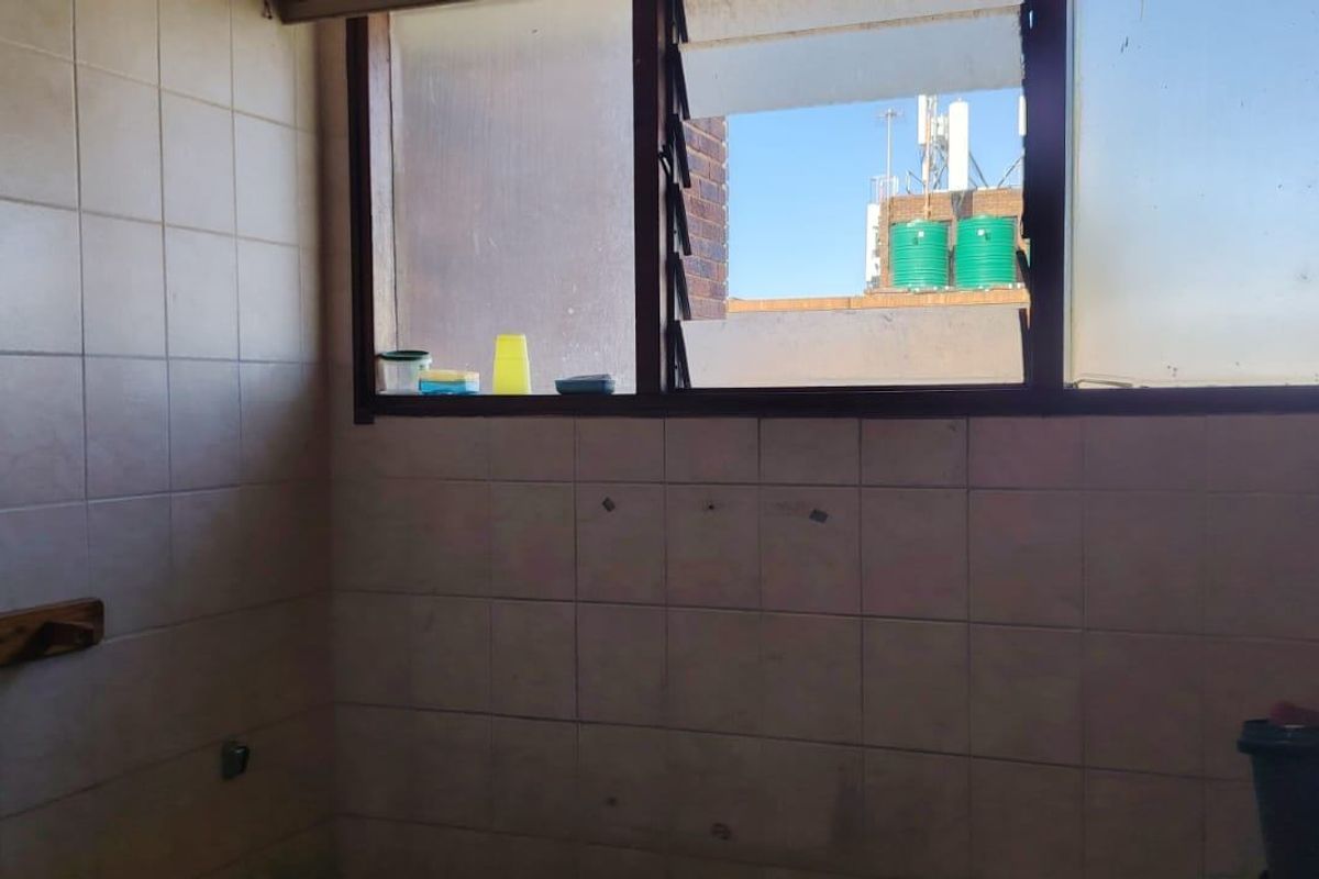 A vacant kitchen area featuring tiled walls and louvered windows, requiring renovation to update the dated finishes and improve the overall condition.