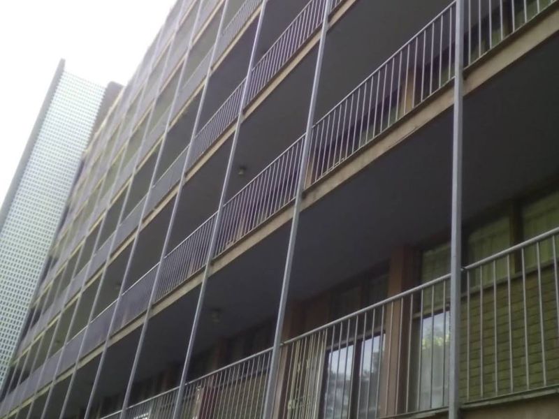 Exterior view of a multi-story apartment building featuring stacked balconies with metal railings and sliding glass door access.