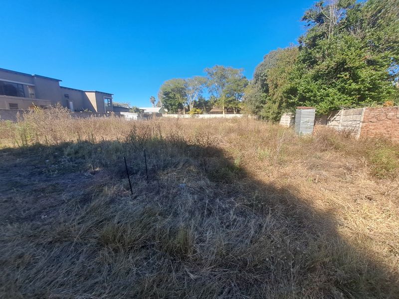 A vacant residential plot featuring overgrown vegetation, enclosed by perimeter boundary walls, offering a blank canvas for future development.