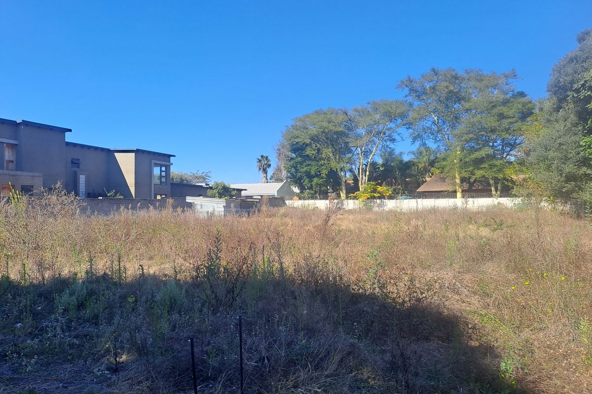 A vacant residential plot featuring level ground, perimeter boundary walls, and established trees, offering a blank canvas for new construction.