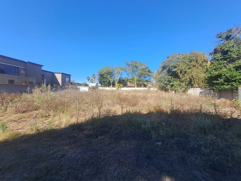 A vacant residential plot featuring overgrown vegetation, enclosed by perimeter boundary walls, offering a blank canvas for future development.
