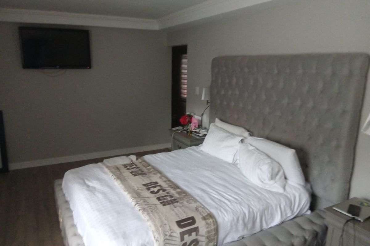 A spacious bedroom featuring neutral wall tones, crown molding, and laminate flooring, equipped with a wall-mounted television.