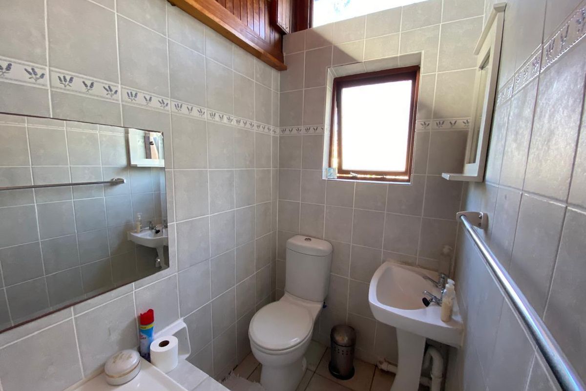 A functional bathroom featuring tiled walls, a pedestal basin, and a toilet, with timber ceiling detailing and natural light from a casement window.