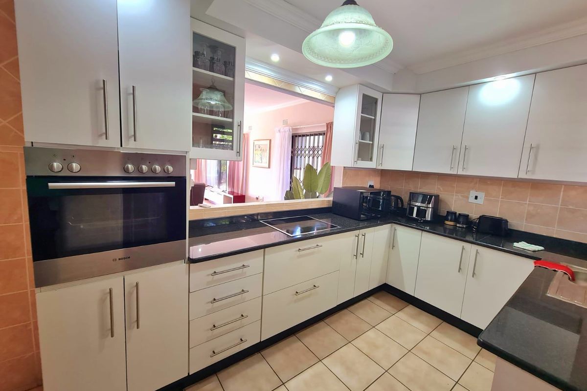 A functional kitchen featuring white cabinetry, dark granite countertops, a built-in Bosch oven, and a convenient serving hatch opening to the living area.
