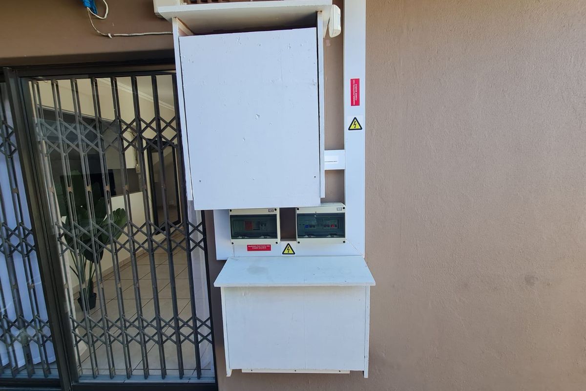 Exterior wall featuring a mounted electrical distribution board and utility housing adjacent to a sliding glass door with a security gate.