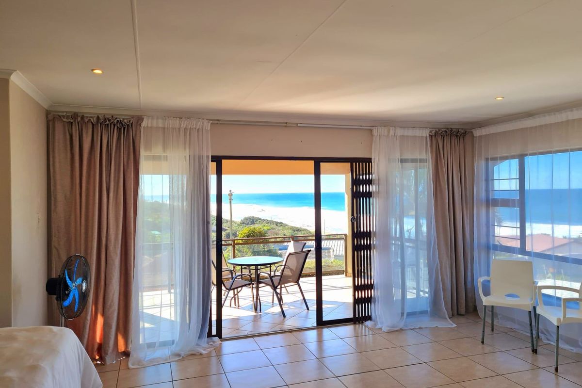 Spacious living area featuring large sliding glass doors that open onto a balcony with scenic ocean views and tiled flooring throughout.