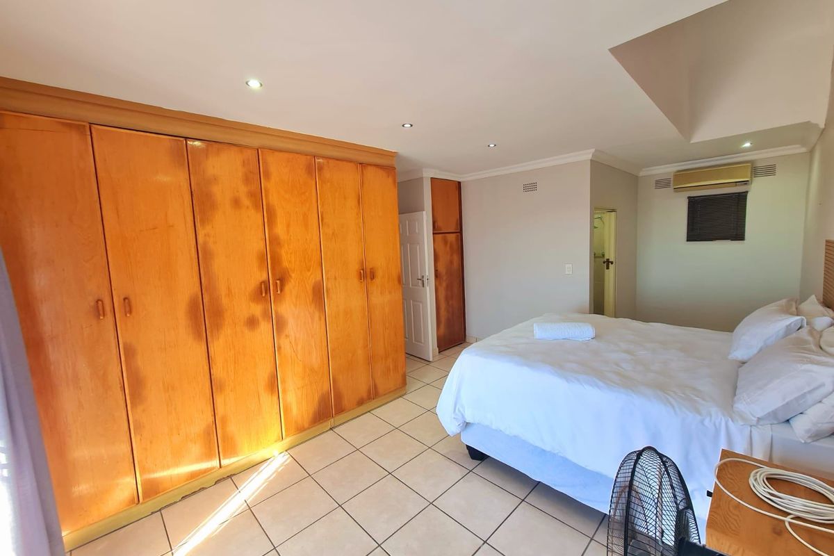 Spacious bedroom featuring extensive built-in wooden cabinetry, tiled flooring, recessed lighting, and an en-suite bathroom access.