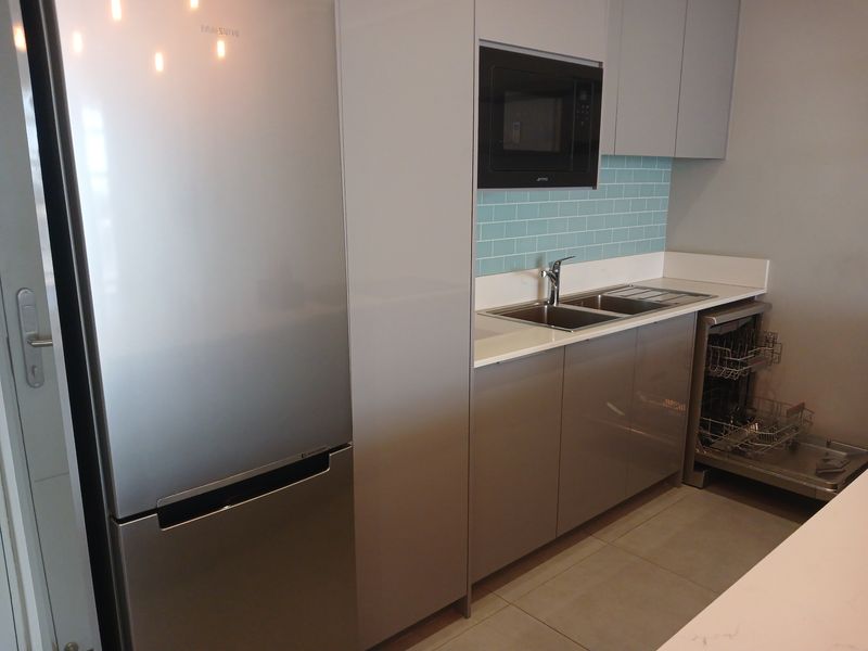 Modern kitchen featuring sleek grey cabinetry, a subway tile backsplash, integrated microwave, stainless steel sink, and a built-in dishwasher.