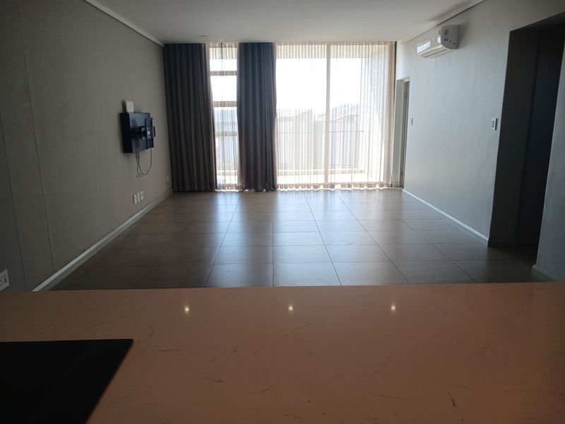 Spacious open-plan living area featuring large floor-to-ceiling windows, tiled flooring, and a wall-mounted air conditioning unit.