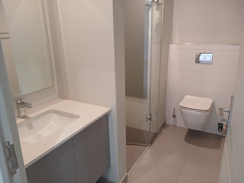 Modern bathroom featuring a wall-mounted toilet, glass-enclosed shower, and a sleek vanity with a basin and mirror.