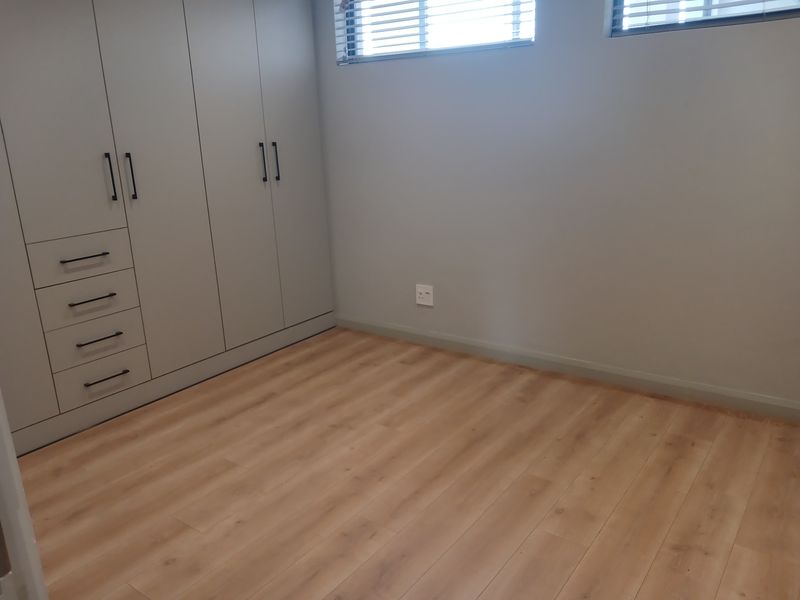 A clean, modern bedroom featuring light wood-look laminate flooring and extensive built-in cabinetry with sleek handles and neutral finishes.