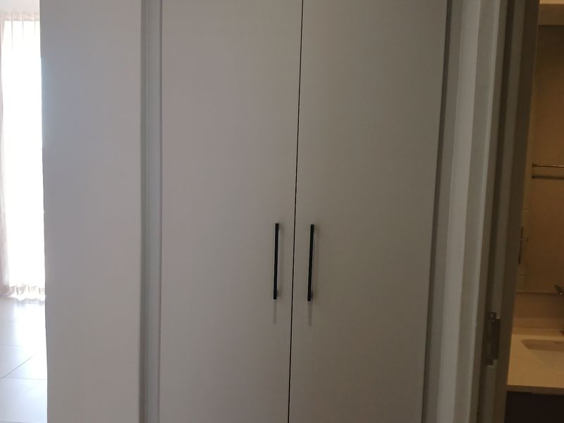 A hallway featuring built-in floor-to-ceiling storage cabinetry with modern matte black handles, providing clean and functional storage space.
