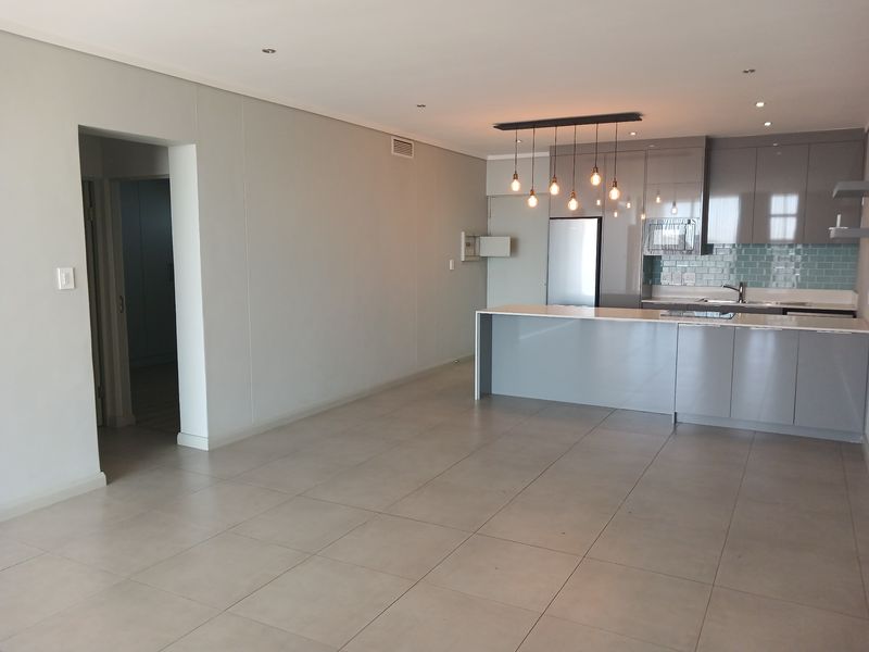 Modern open-plan kitchen and living area featuring sleek grey cabinetry, a central island, tiled flooring, and contemporary pendant lighting.