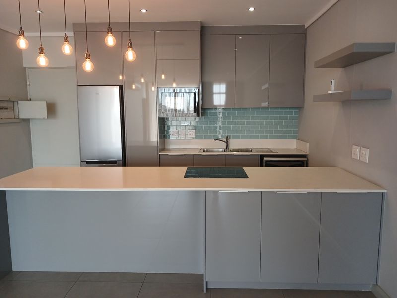 Modern kitchen featuring sleek grey cabinetry, a central island with a built-in cooktop, quartz countertops, and a stylish subway tile backsplash.