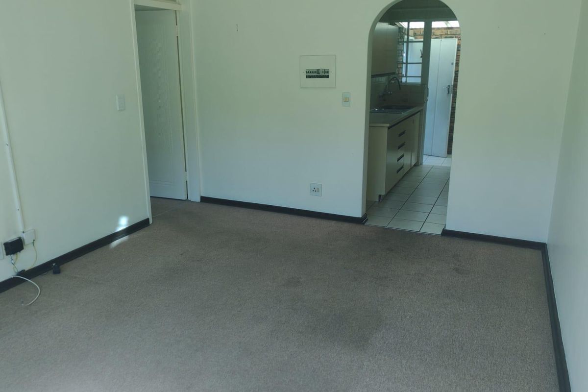 An empty living area featuring neutral carpeting and an arched doorway leading to a functional kitchen space.
