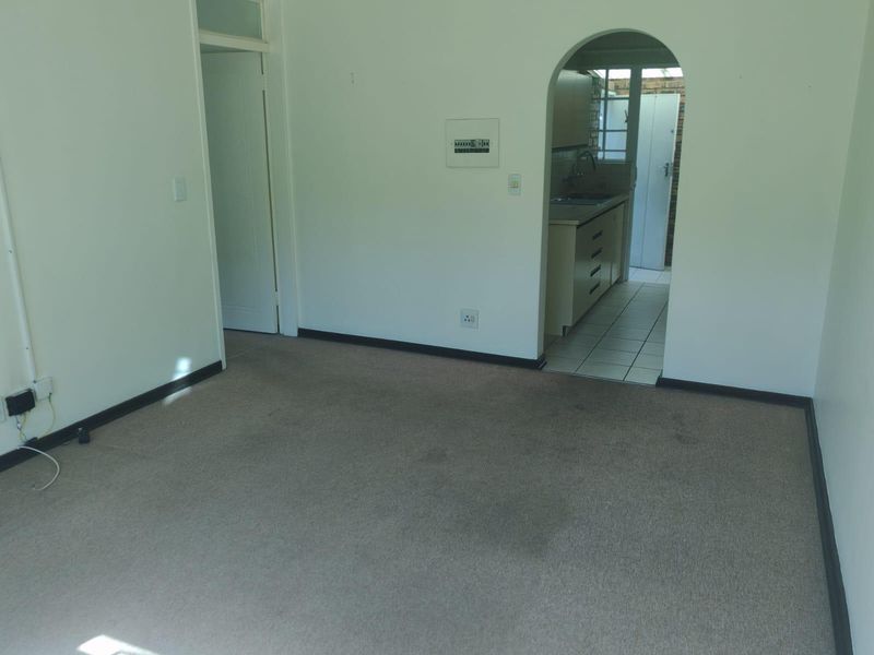 An empty living area featuring neutral carpeting and an arched doorway leading to a functional kitchen space.