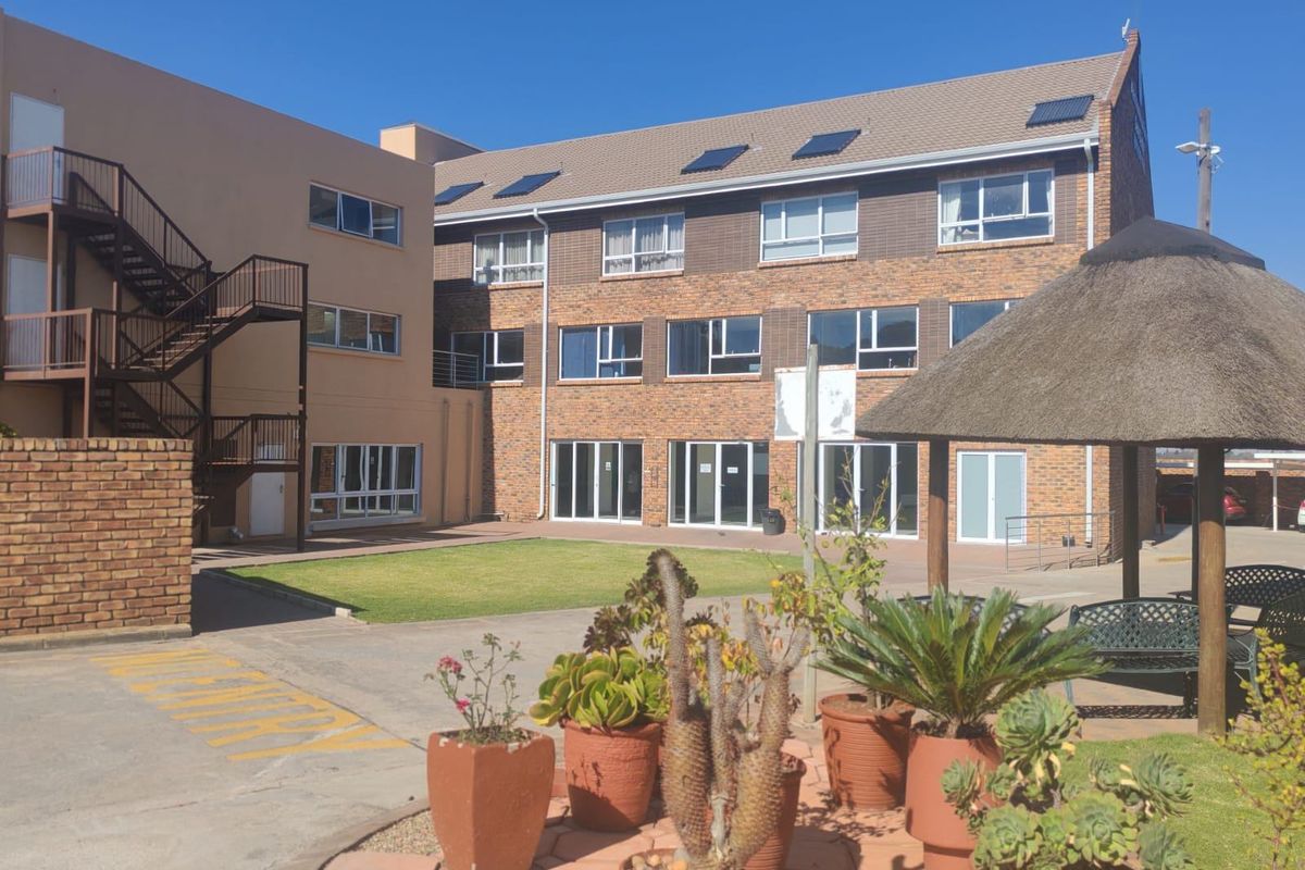 Exterior view of the apartment complex featuring a central courtyard, landscaped garden, thatched gazebo, and external metal staircases.