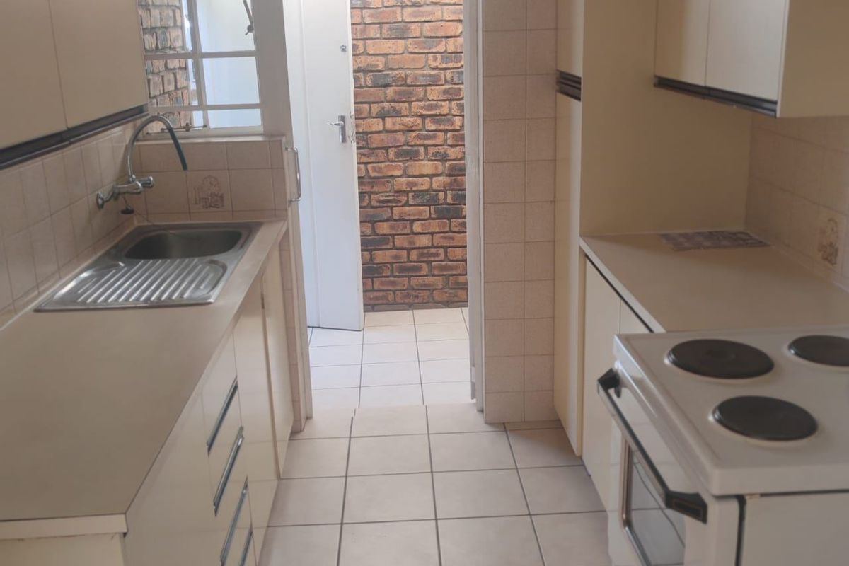 A functional galley-style kitchen featuring tiled flooring, built-in cabinetry, a stainless steel sink, and a freestanding electric stove, with direct access to an outdoor area.