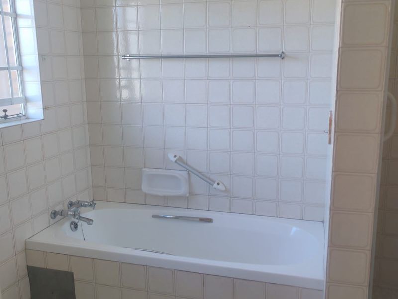 A functional bathroom featuring a built-in bathtub with chrome fixtures, wall-mounted grab rail, and tiled wall and floor finishes.