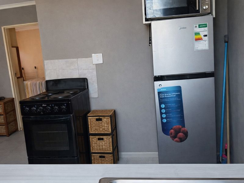 A functional kitchen area featuring a freestanding electric stove, tiled splashback, and space for a refrigerator with an integrated microwave shelf.
