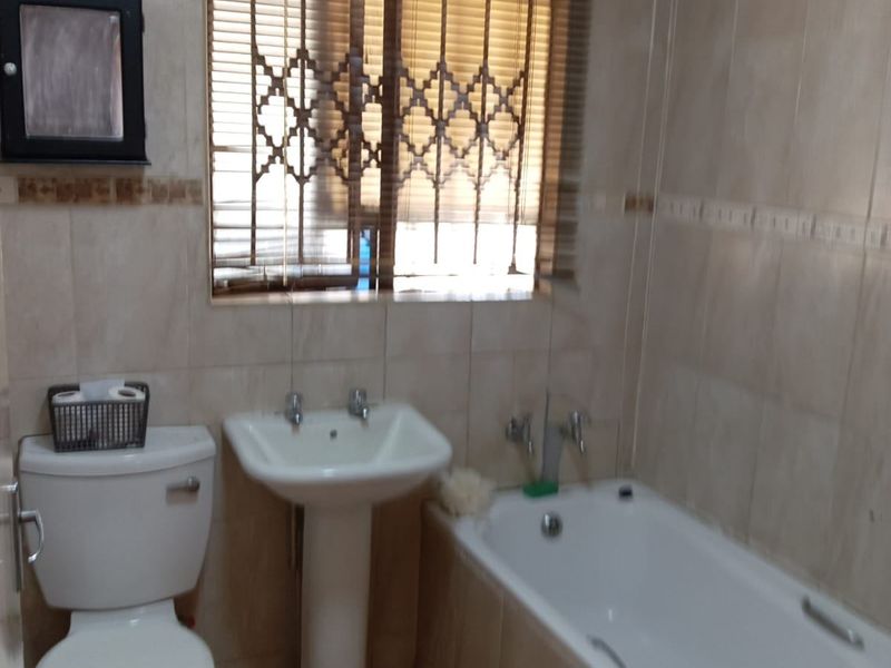 A functional bathroom featuring a standard bathtub, pedestal basin, and toilet, finished with neutral wall and floor tiling.